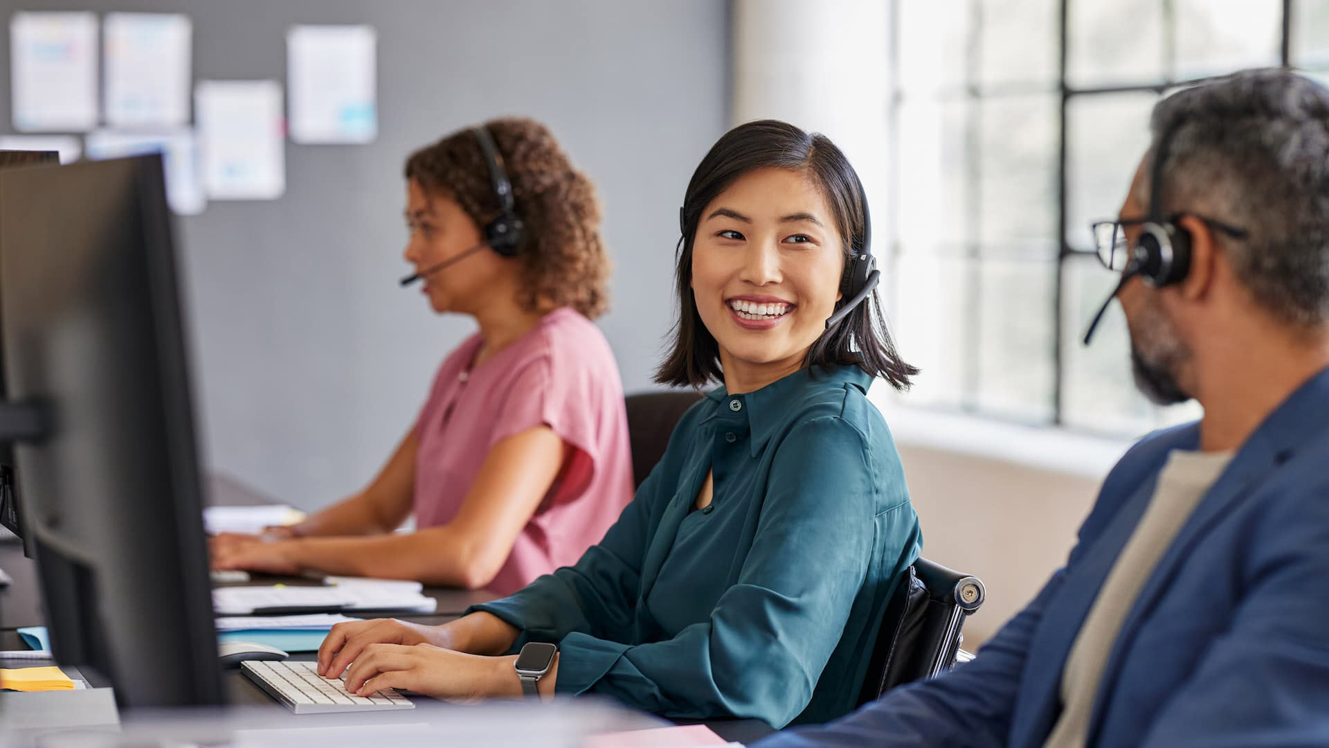 A contact center representative smiles at her peers while wearing a headset.