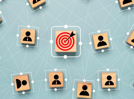 Network of wooden blocks with user icons connected by lines, with a central block showing a red target and arrow.