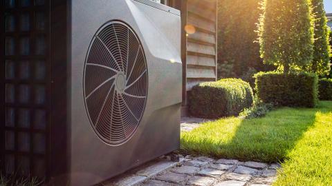 Outdoor heat pump unit next to a house with green lawn and shrubs