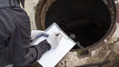 Person writing on a clipboard while inspecting an open manhole
