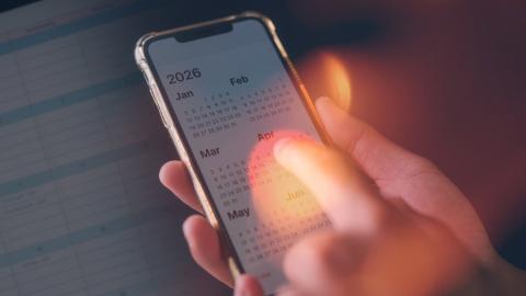 Hand with pointer finger hovering over a phone displaying calendar year 2026.